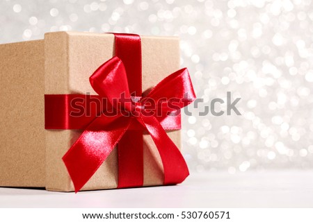 Present box with red bow on silver sparkling background. Festive concept for Christmas
