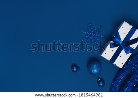 Present box wrapped with a ribbon, decorative balls and snowflake on colorful paper background. Christmas gift. Holiday concept. Image is with copy space. Flat lay. Top view