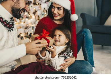 Present For A Dad. Christmas Morning Celebration, Mom And Little Daughter Give Gift Box Container To Father. Enjoing Holidays Family People