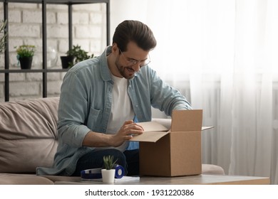 Present from distant friend. Happy millennial man unpack open box with birthday gift surprise received by mail. Smiling young guy has pleasure to receive package with consumer goods purchased online