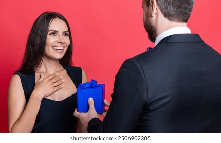 Present. Man making proposal to woman. Man give present gift box for Valentines day to woman. Happy Valentines day. Couple in love isolated on red. Romantic proposal with gift. Tandem present - Powered by Shutterstock