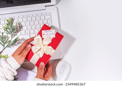 Present from secret santa on workplace table. Office Christmas and New Year celebration game. Office table surface, notebook with festive gift box, white background flatlay copy space - Powered by Shutterstock