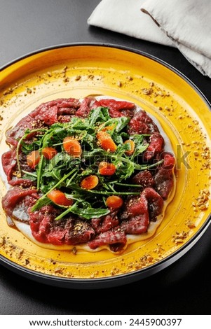 presentation of Beef Carpaccio with celery sauce, garnished with arugula, served on a black table.
