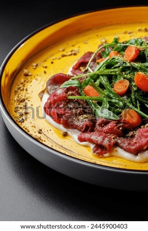 presentation of Beef Carpaccio with celery sauce, garnished with arugula, served on a black table.