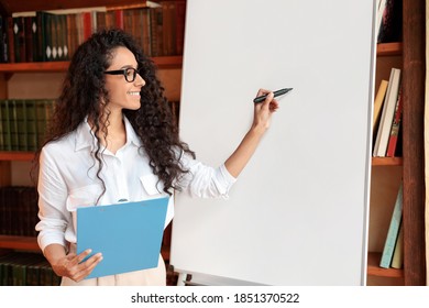 Presentation Concept. Portrait of smiling professional female manager in eyeglasses posing near blank empty whiteboard. Woman in white shirt standing with marker and writing on flipchart, copy space
