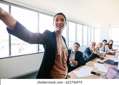 Presentation In Modern Conference Room With Asian Businesswoman Showing Something Important To Colleagues Sitting Back. Mature Asian Woman Presenting Her Ideas To Colleagues