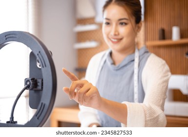 Presentation of new line of clothing online. Smiling asian business woman fashion designer makes video for advertising clothes in tailor shop home office studio interior - Powered by Shutterstock