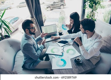 Presentation Of A New Start Up For Investors. Three Young Successful People Are Discussing Numbers In A Nice Light Modern Coworking, All In Formal Wear, Concentreted