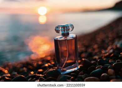 Presentation Of The Summer Fragrance. A Glass Bottle Of Golden Perfume On A Pebble Beach, Against The Sunset. The Concept Of Selective Perfumery And The Fashionable Luxury Industry.