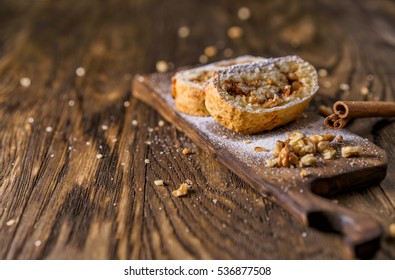 Presentations portion of apple strudel on a wooden board, beside lies cinnamon stick.