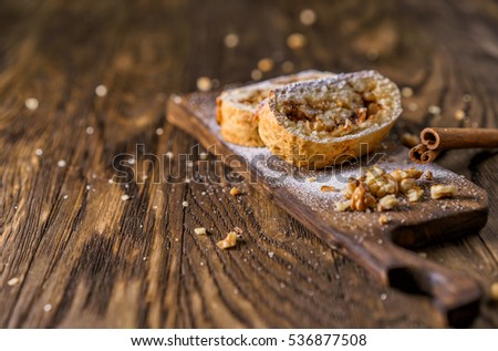 Presentations portion of apple strudel on a wooden board, beside lies cinnamon stick.