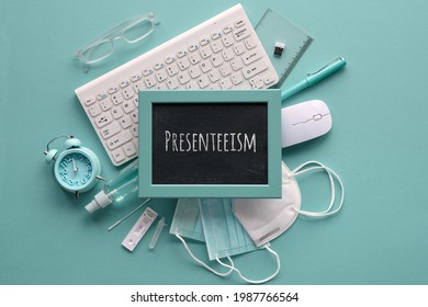 Presenteeism Term Written On Blackboard. Flat Lay In Monochrome Mint Blue Hues. Office Supplies, Keyboard, Mouse, Alarm Clock, Pens, Glasses, Covid Test, Medical Masks. Overworking At Workplace.