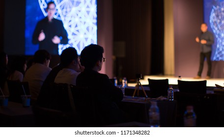 Presenter Giving Presentation To Group Of People From Stage At Conference Event. Trainer Speaker Giving Lecture Speech. Teacher Education On Business And Technology. Blurred.