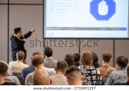 Presenter points to screen, audience seated, conference room in focus, professional seminar atmosphere