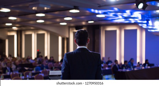 Presenter Presenting Presentation To Audience. Defocused Blurred Conference Meeting People. Lecturer On Stage. Speaker Giving Speech To People.