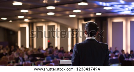 Presenter Presenting Presentation to Audience. Defocused Blurred Conference Meeting People. Lecturer on Stage. Speaker Giving Speech to Audience in Conference Hall Auditorium. Forum for Professionals
