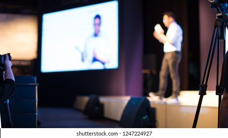 Presenter Presenting Presentation To Conference Audience. De-focused Blurred . Lecturer On Stage At Tech Forum. Speaker Giving Speech In Conference Hall Auditorium. Copy Space Screen Background.