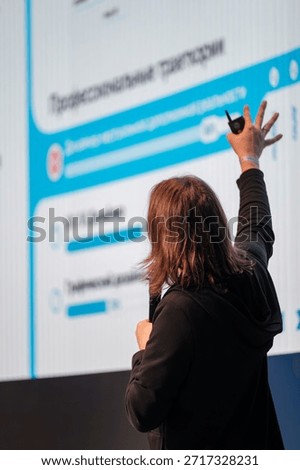 Presenter stands before large screen showcasing charts during conference, pointing with laser device, engaging audience and sharing insights.
