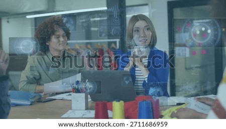 Presenting designer in blue blazer gesturing, explaining designs at studio with laptop, fabric, HUD. Collaboration, fashion, atelier, sketches, swatches, dressform, patterns