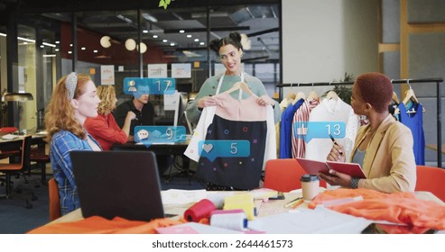 Presenting designer holding two-tone dress on hanger in open-plan workspace, with social icons. Creative, teamwork, fashion, innovative, contemporary, collaborative, aesthetic