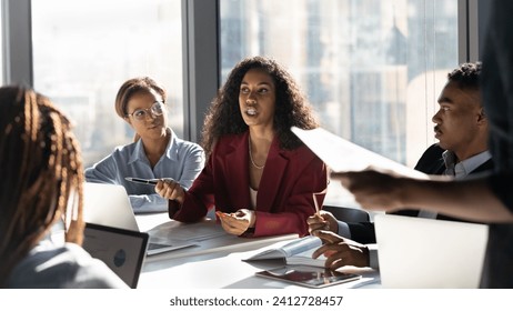 Presenting idea. Inspired black african woman employee propose marketing plan to interested diverse colleagues on briefing. Young biracial female manager expert talk to teammates express point of view - Powered by Shutterstock