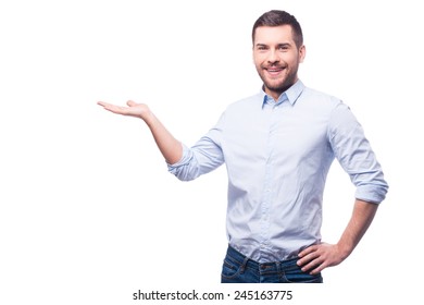 Presenting new project. Handsome young man in shirt looking at camera and holding copy space while standing against white background 