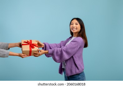 Presents Delivery, Birthday And New Year Holiday Celebration Concept. Happy Asian Lady Receiving Wrapped Gift Box, Standing Over Blue Studio Background And Smiling To Camera