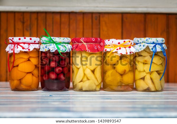 Preserved food in jar, fruit compote on wooden\
table. Variety of homemade preserved fruit in kitchen. Apricot,\
cherry, pear, plum and apple\
compotes