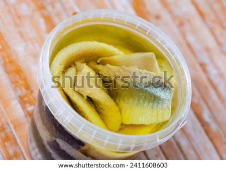 Preserved herring fillet in round plastic container served for consumption on the laid table