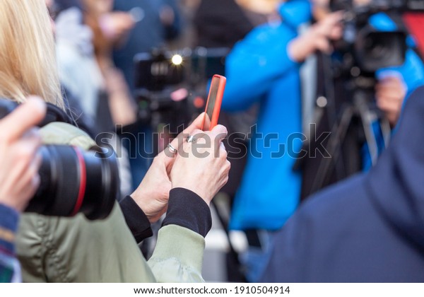 Press or news conference, mobile journalist\
filming media event with a\
smartphone