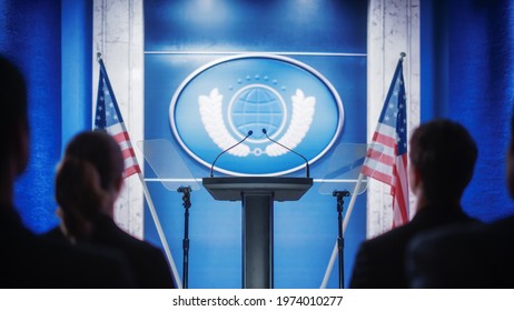 Press Representatives Waiting For A Political Conference To Start. Media Pool Of Journalists And Photographers Sitting Before The Party Stage With Tribune Podium And Backdrop With American Flags.