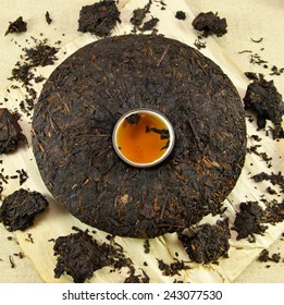 Pressed cake of Asian pu-erh tea with clay cup full of hot tea in the middle, on paper background 