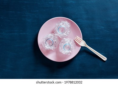 Pressed Plastic Water Bottles On A Plate With A Plastic Fork. Microplastics In Food, Nutrition, Health And Environmental Pollution Or Safety Concept.