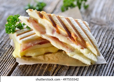 Doppel-Panini mit Schinken und Käse auf Sandwich-Papier auf Holztisch gepresst und geröstet