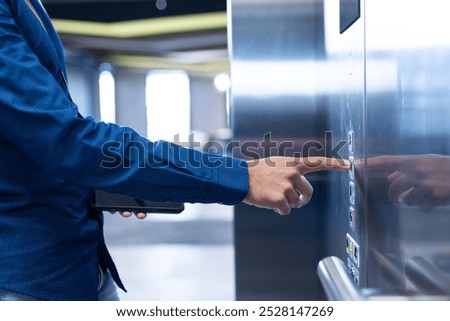 Pressing elevator button, person in blue shirt holding tablet in modern office. Corporate, business, technology, professional, work, interior
