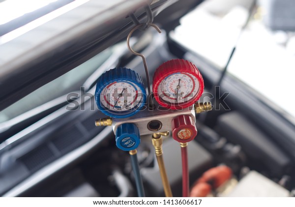 Pressure gauge is hanged on\
the hood over the engine for measuring the refrigerant pressure due\
to air condition in the car is not working. Car service\
concept.