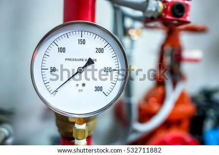 pressure gauge psi meter in pipe and valves of fire emergency system industry focus closeup middle red background