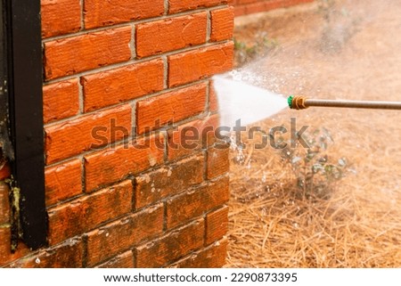 Pressure washer using water to clean a dirty brick wall on a house.