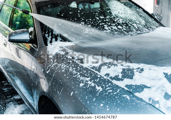 pressure\
washer with water on grey modern car with foam\
