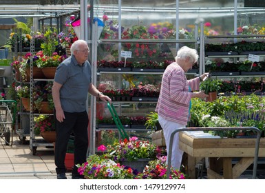 Preston, Lancashire/UK - July 7th 2019: The Garden Centre, Elderly Caucasian Couple Shopping For Garden Plants And Flowers With Man Pushing Trolley And Woman Looking At A Plant Label