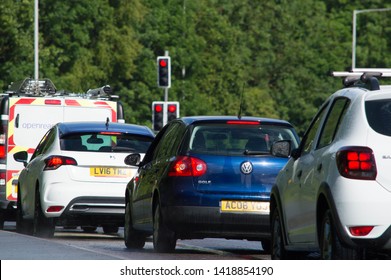 Preston, Lancashire/UK: June 6th 2019:  A Line Of Cars Waiting At Red Traffic Lights With Green Trees In The Background