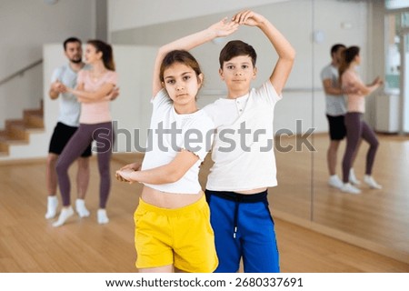 Pre-tee siblings practicing active dance in pair during family dance class, parents dancing on background