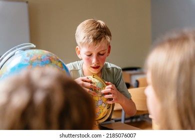 Preteen blond boy with rosy cheeks focused on looking for a country on the globesitting in the classroom at a geography lesson at school. - Powered by Shutterstock