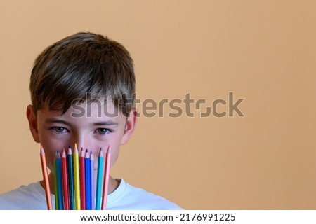 Preteen boy with colored pencils on his face with orange background. Concept of back to school