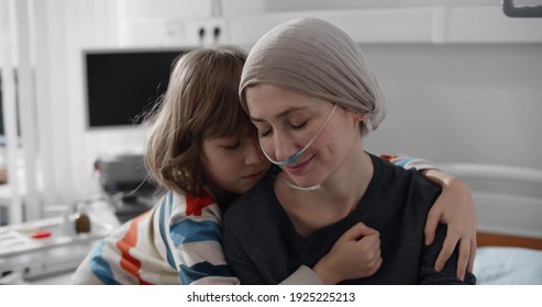 Preteen boy embracing sick mother with cancer in hospital bed. Portrait of ill woman patient in headscarf after chemotherapy hugging little son visiting her in ward