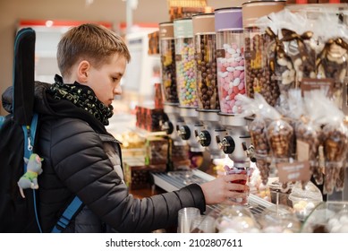Preteen boy filling a jar with candies in the confectionery. Boy buying sweets in the candy shop.