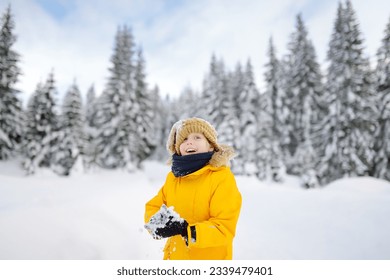 Preteen boy having fun playing with fresh snow during vacation in european Alps. Child dressed in warm clothes, hat, hand gloves and scarf. Active winter outdoors leisure for kids on holidays time - Powered by Shutterstock