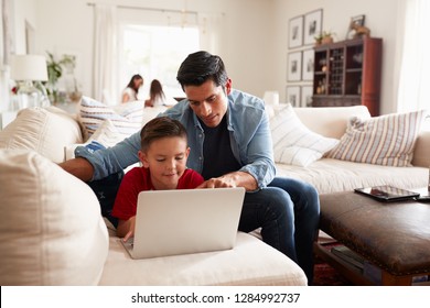 Pre-teen boy lying on sofa using laptop, dad sitting beside him, mum and sister in the background