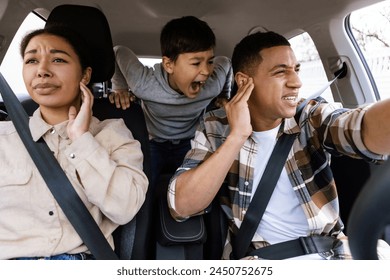 Preteen boy shouting, feeling angry, parents covering ears while travelling together by car, having family conflicts during car trip - Powered by Shutterstock