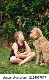 Pre-teen Boy Sitting On Grass Playing With Large Happy Golden Doodle Dog